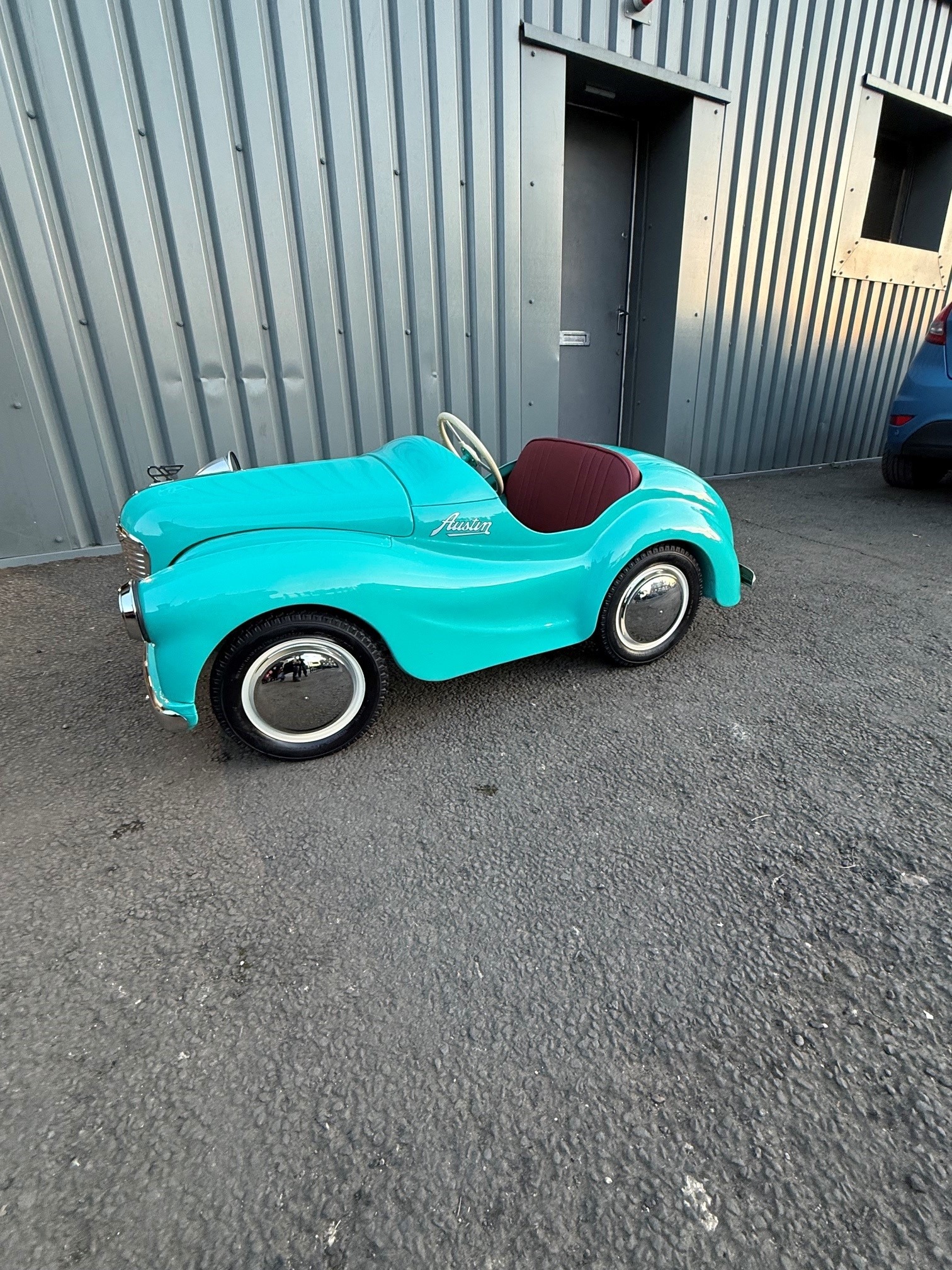 Small turquoise classic vehicle beside the JRM Coachworks workshop